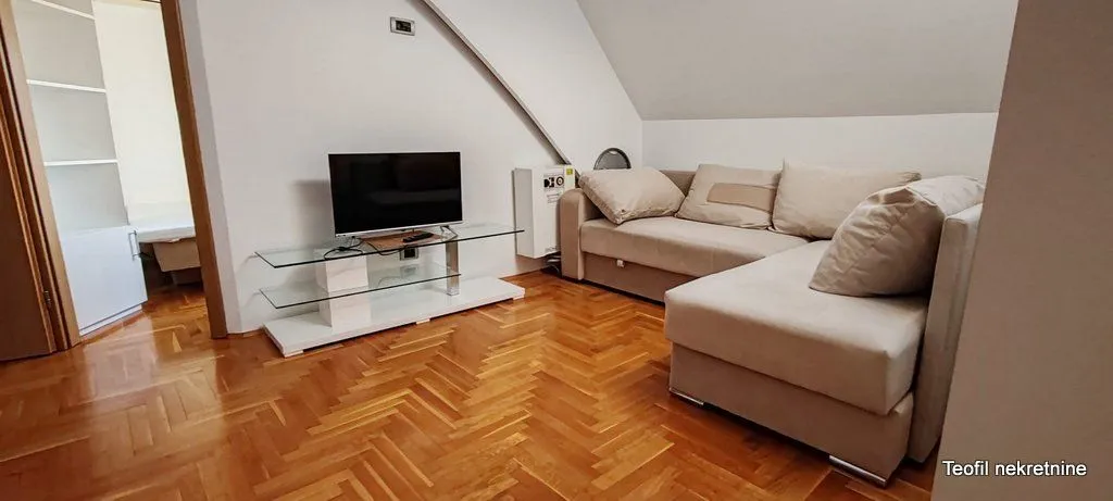 Living room with a sectional sofa, television, and hardwood flooring.