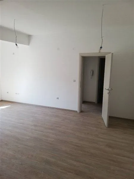 Prazna soba sa svijetlim laminatom i bijelim zidovima.