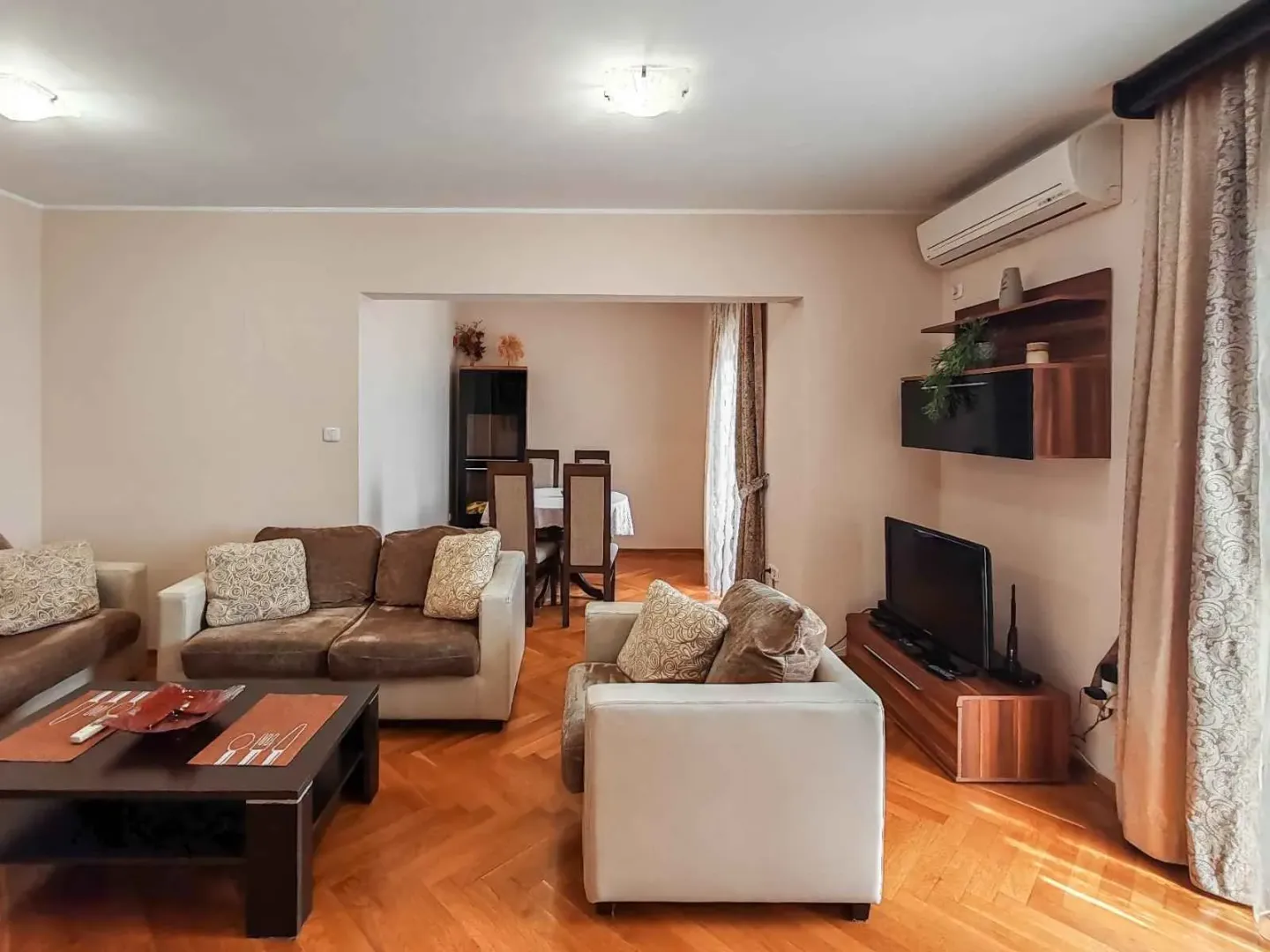 Living room with seating area, TV, and dining area in the background.