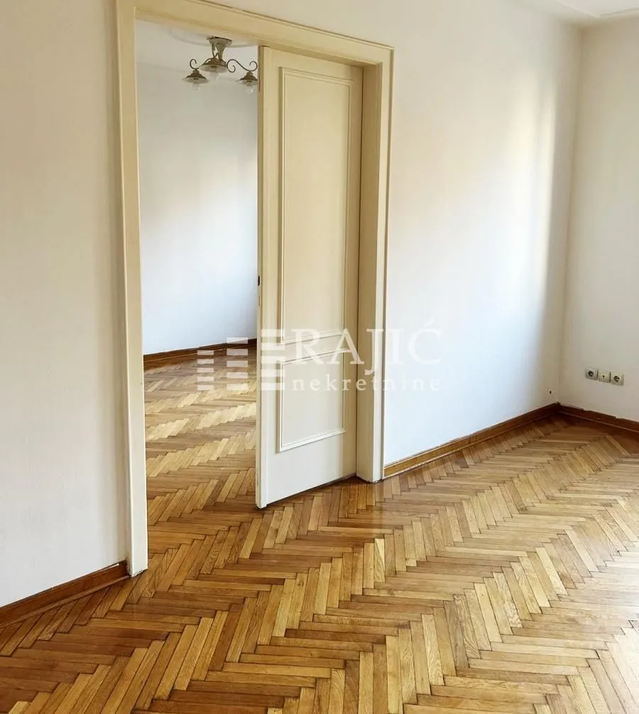 Empty room with wooden parquet flooring and an open door.