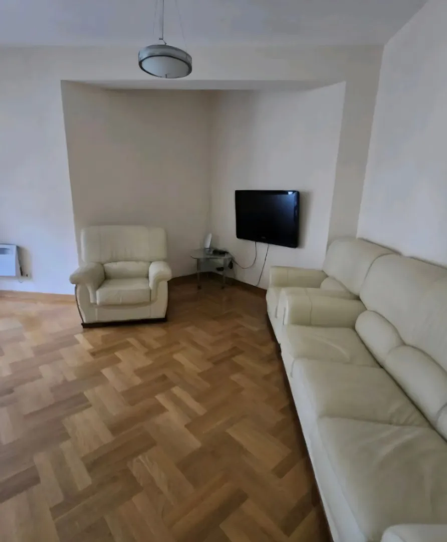Living room with white sofa set and parquet flooring.