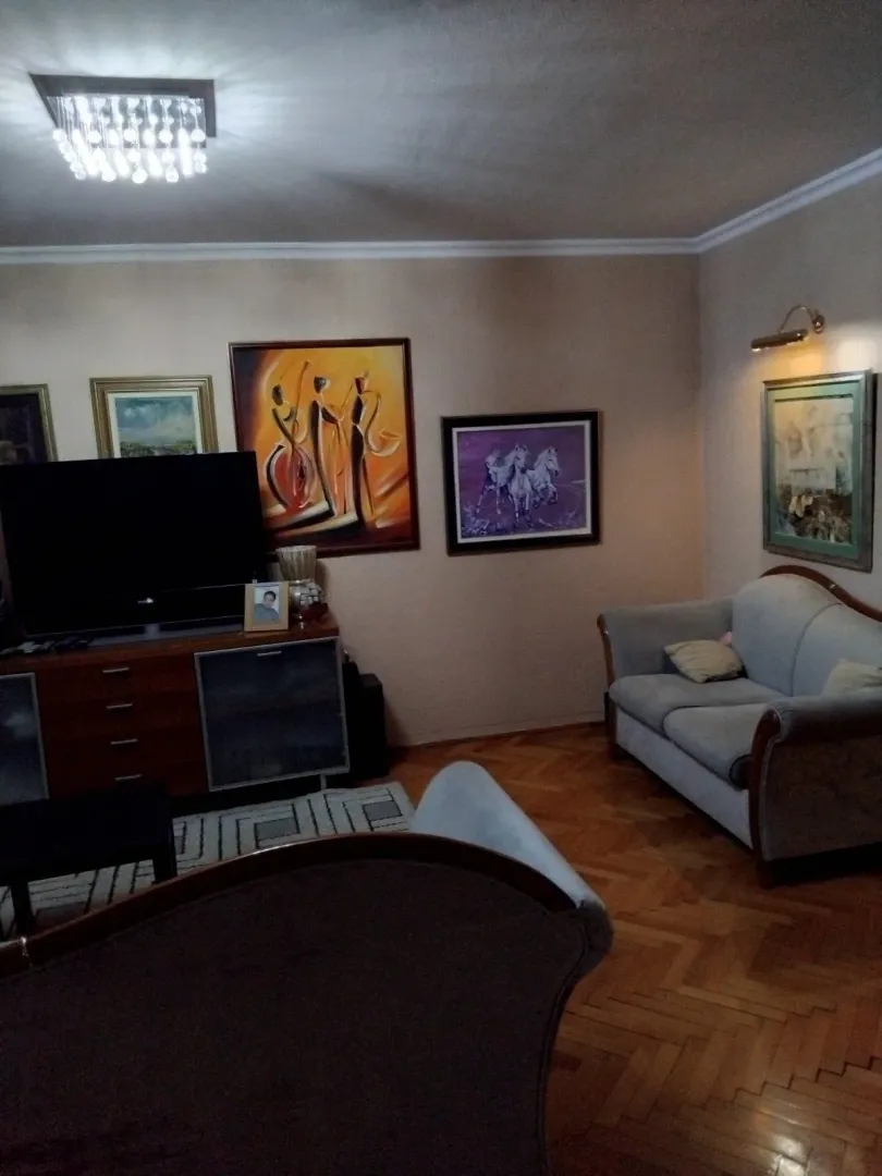 Dnevna soba sa garniturom za sjedenje, televizorom i umjetničkim slikama na zidu.