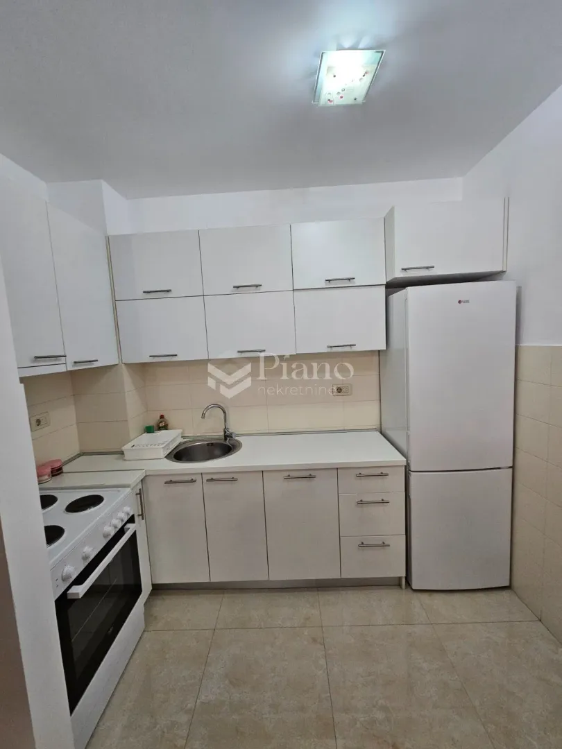 Manja bijela kuhinja sa frižiderom i šporetom.