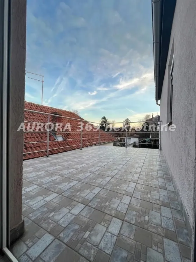 Prostrana popločana terasa sa metalnom ogradom i pogledom na okolinu.