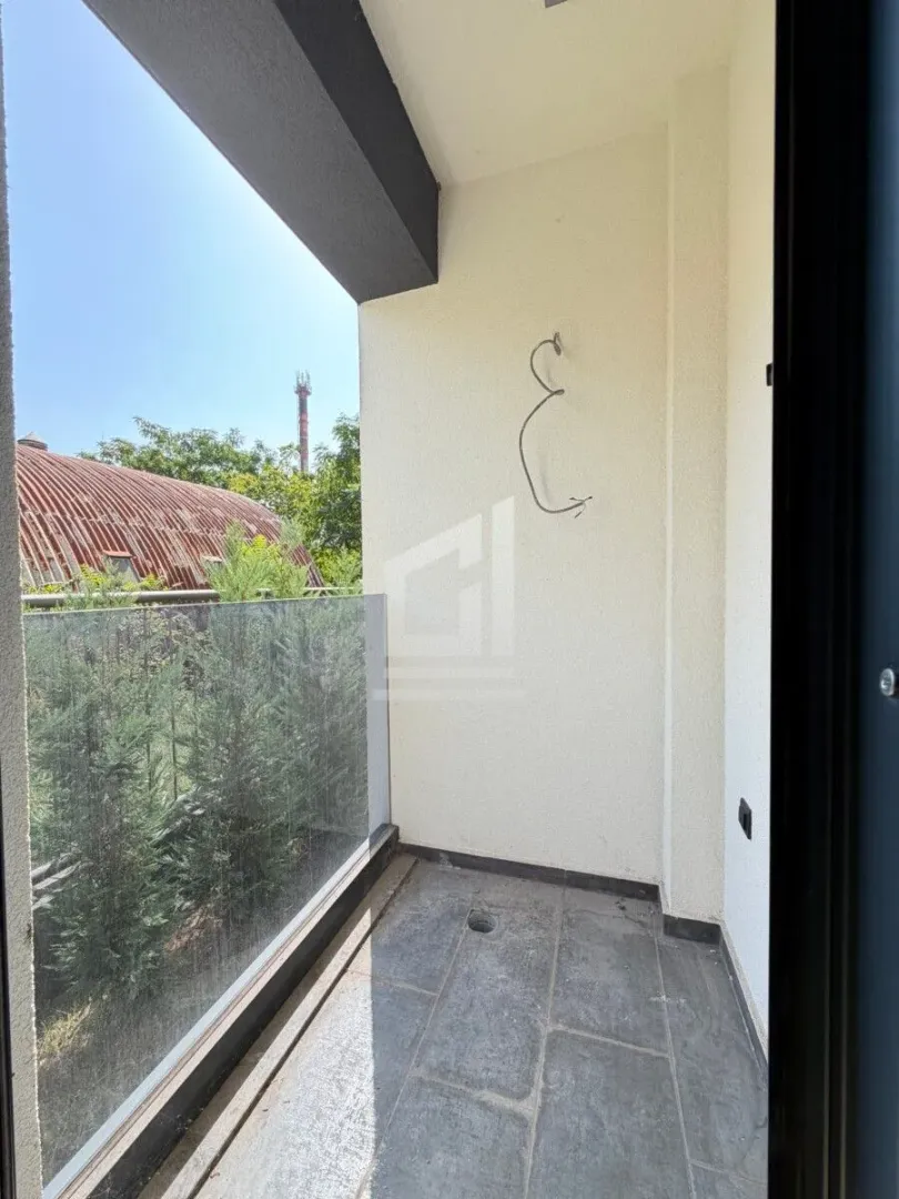 Nenamješten balkon sa staklenom ogradom i pogledom na zelenilo.