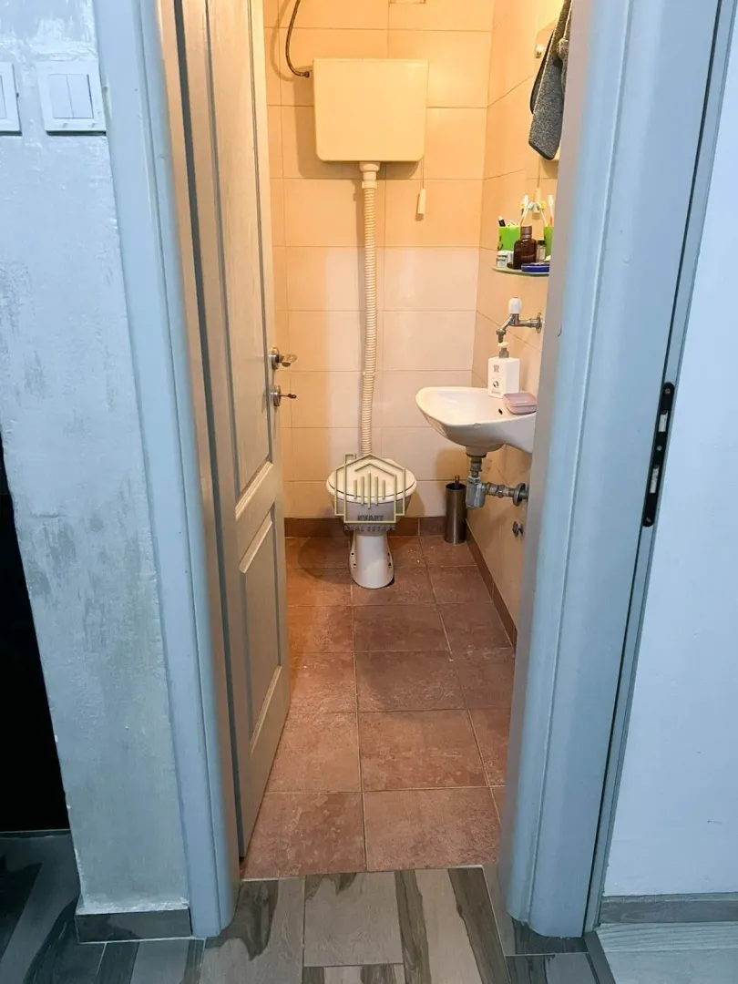 Pogled iz hodnika na manje kupatilo sa WC šoljom i umivaonikom.