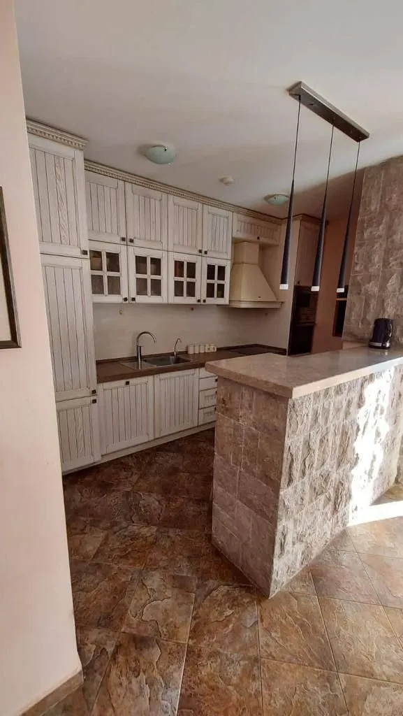 Moderna kuhinja sa bijelim elementima i šankom od kamena.