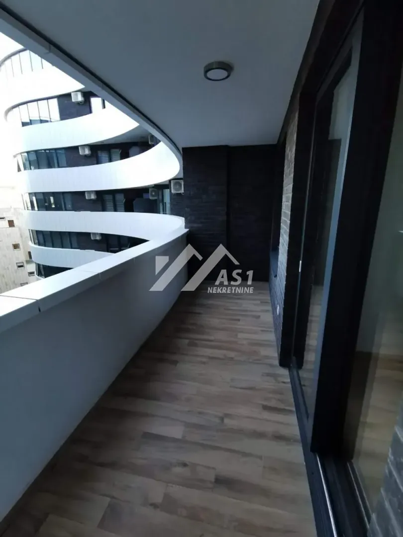 Natkriveni balkon sa drvenim podom i pogledom na zgradu.