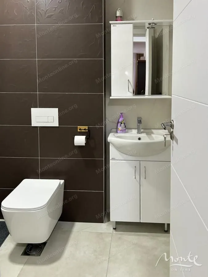 Manje kupatilo sa bijelim umivaonikom, ogledalom i konzolnom wc šoljom.