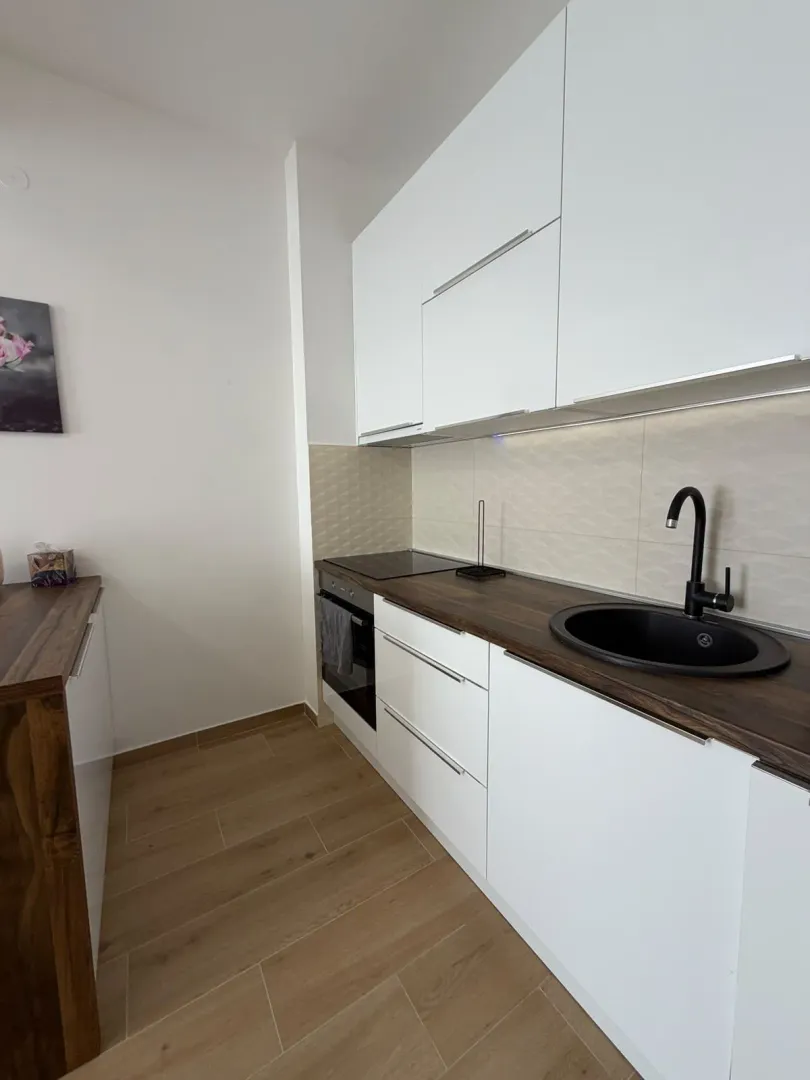 Moderna bijela kuhinja sa tamnom radnom pločom i sudoperom.