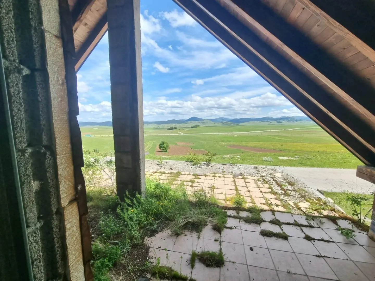 Pogled sa terase na prostrana zelena polja i brda u daljini.