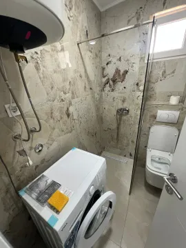 Modern bathroom with a walk-in shower, toilet, and washing machine. - image 8