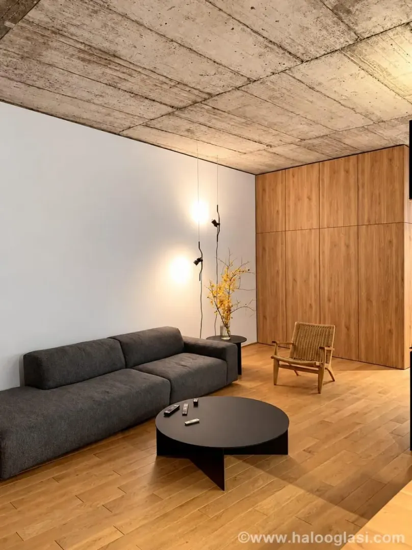 Living room with a sofa, wooden flooring, and a raw concrete ceiling.