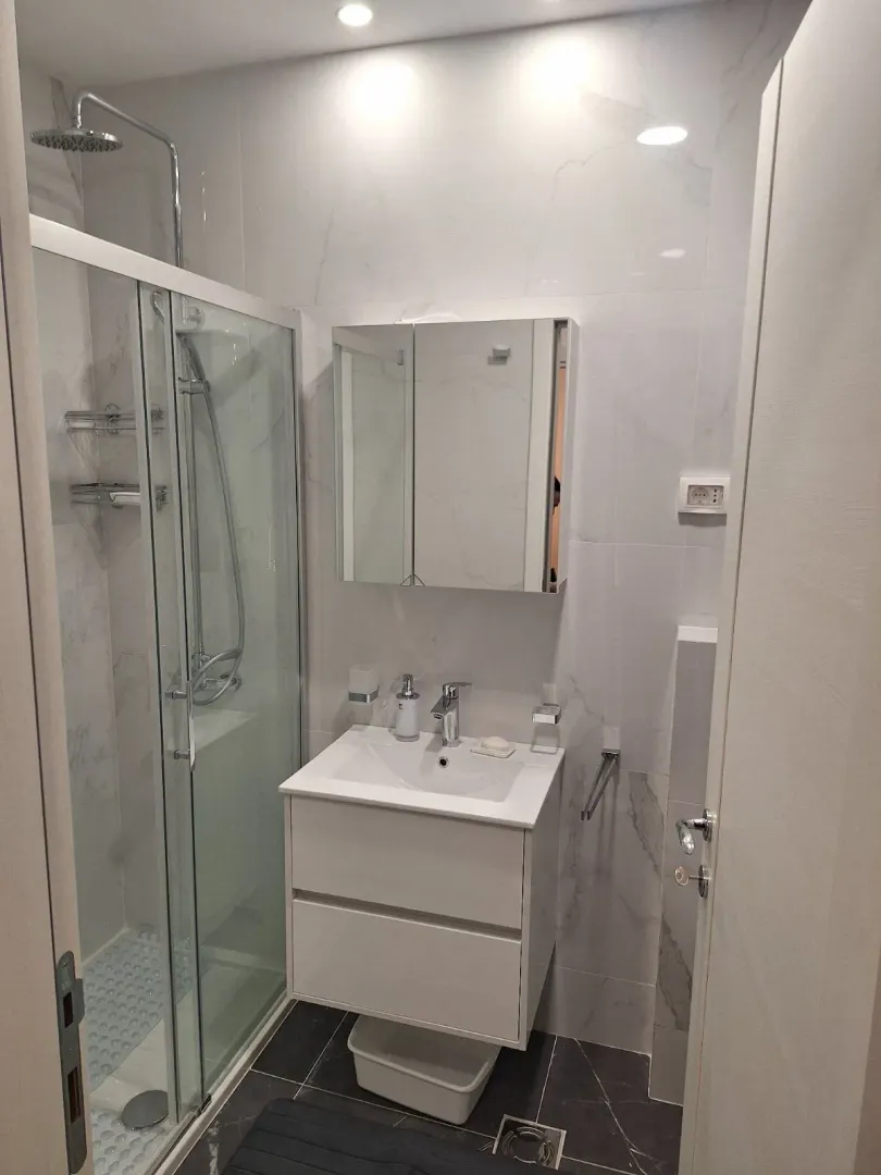 Moderno kupatilo sa tuš kabinom i bijelim lavaboom sa ormarićem.
