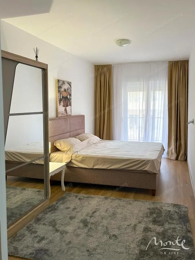 Namještena spavaća soba sa bračnim krevetom, garderoberom i prozorom sa zavjesama.