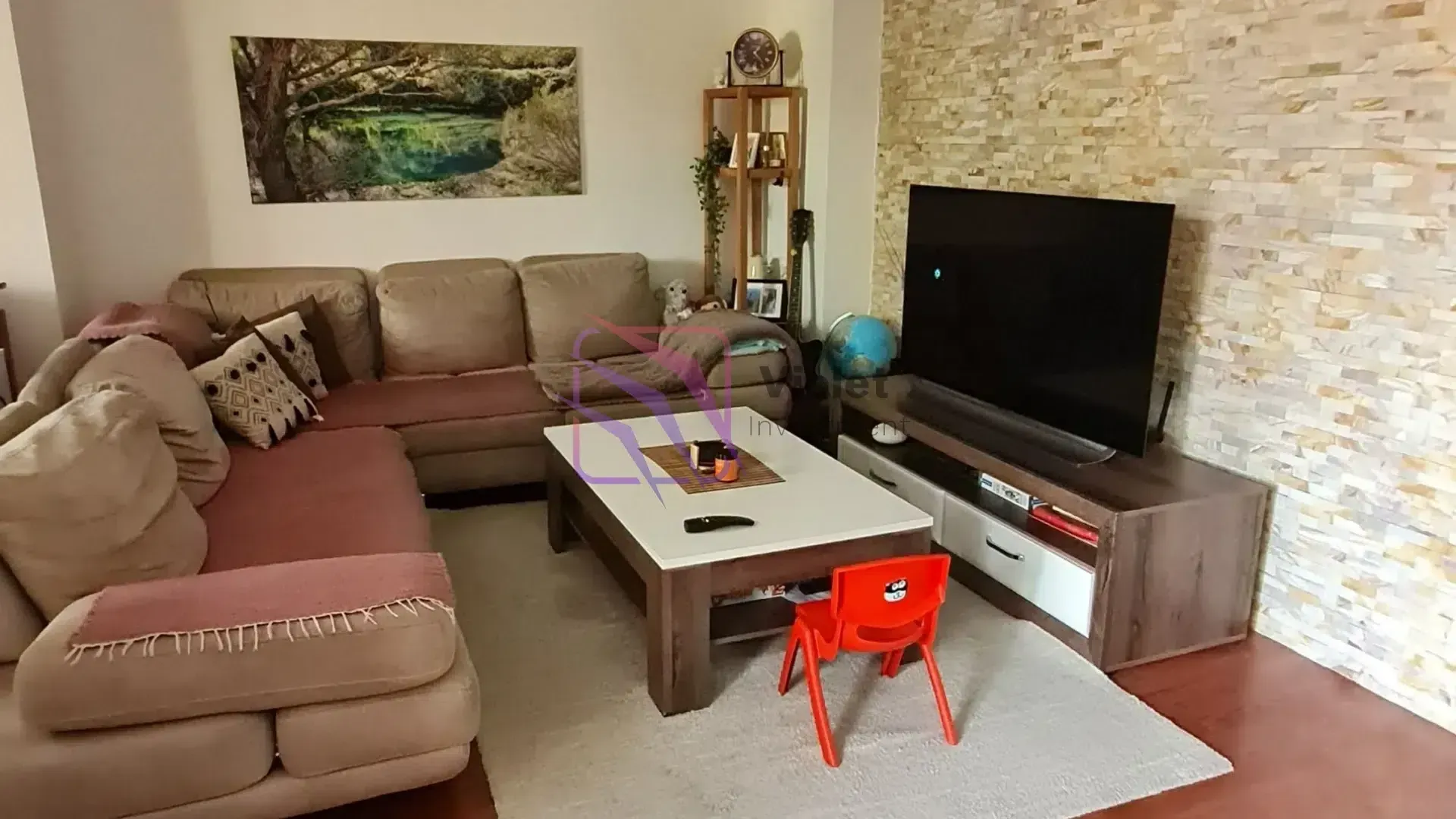 Dnevna soba sa ugaonom garniturom, stočićem i televizorom na zidu od ukrasnog kamena.