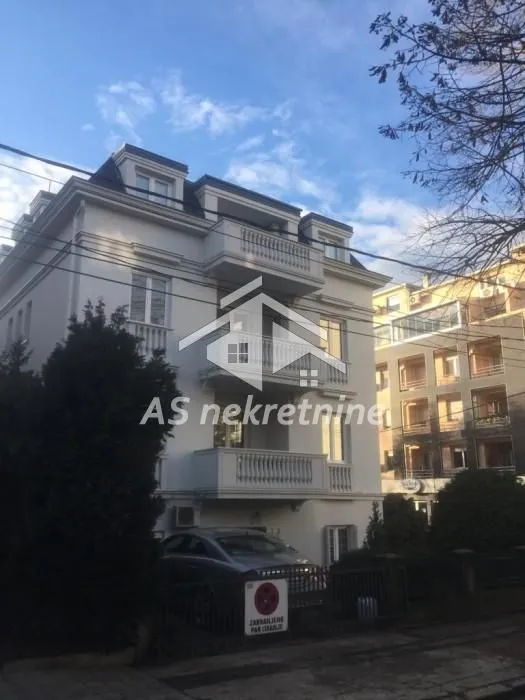 Pogled na spoljašnjost stambene zgrade sa dvorištem i parkingom.
