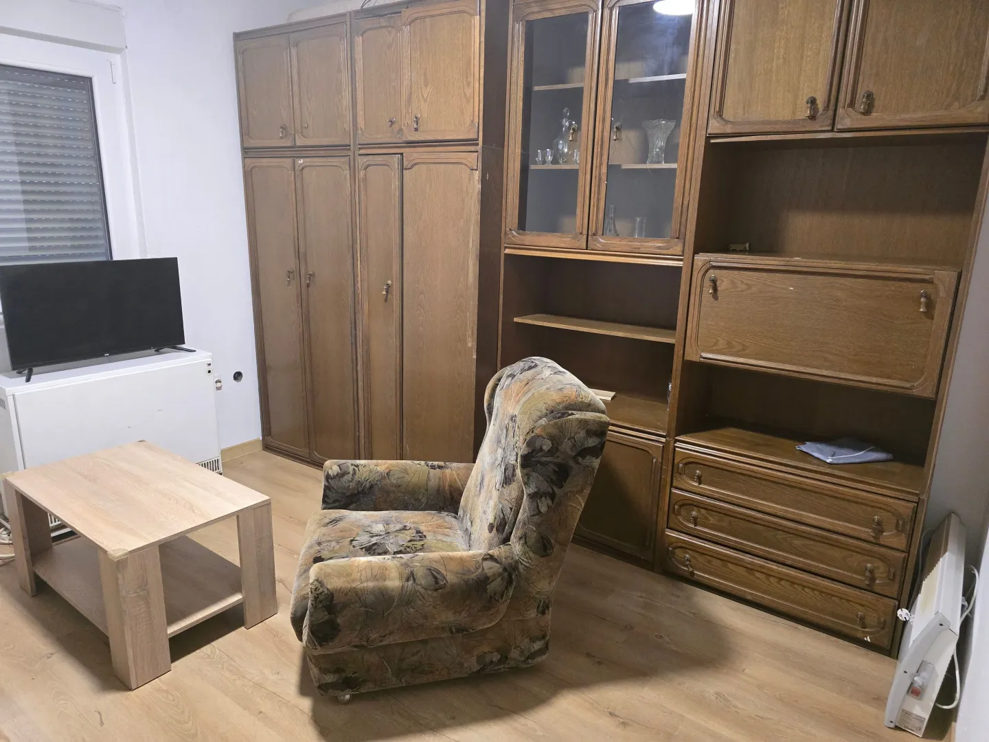 Dnevna soba opremljena drvenim ormanima, foteljom, stočićem i televizorom.