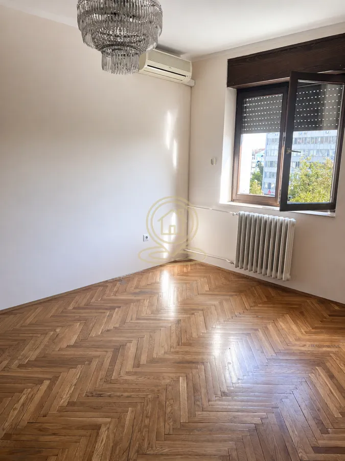 Prazna soba sa parketom, lusterom, klima uređajem i prozorom.