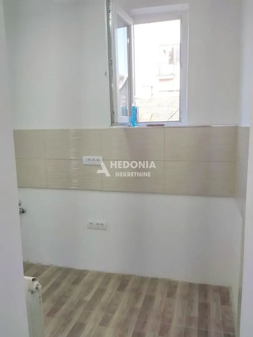 Prazan kuhinjski prostor sa pločicama na zidu i prozorom.