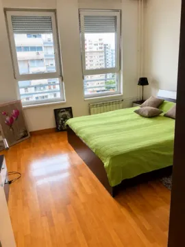 Bedroom with a double bed, wooden floor and two windows with a city view. - image 2