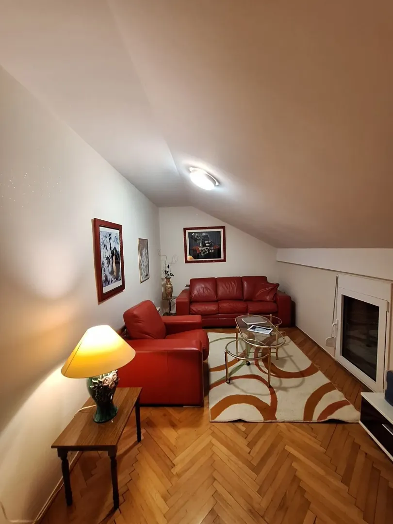 Attic living room with red leather sofas and wooden parquet flooring.