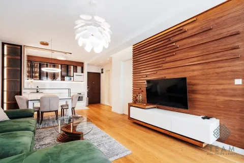Living room with a wooden wall panel, television and a dining area in the background. - image 3