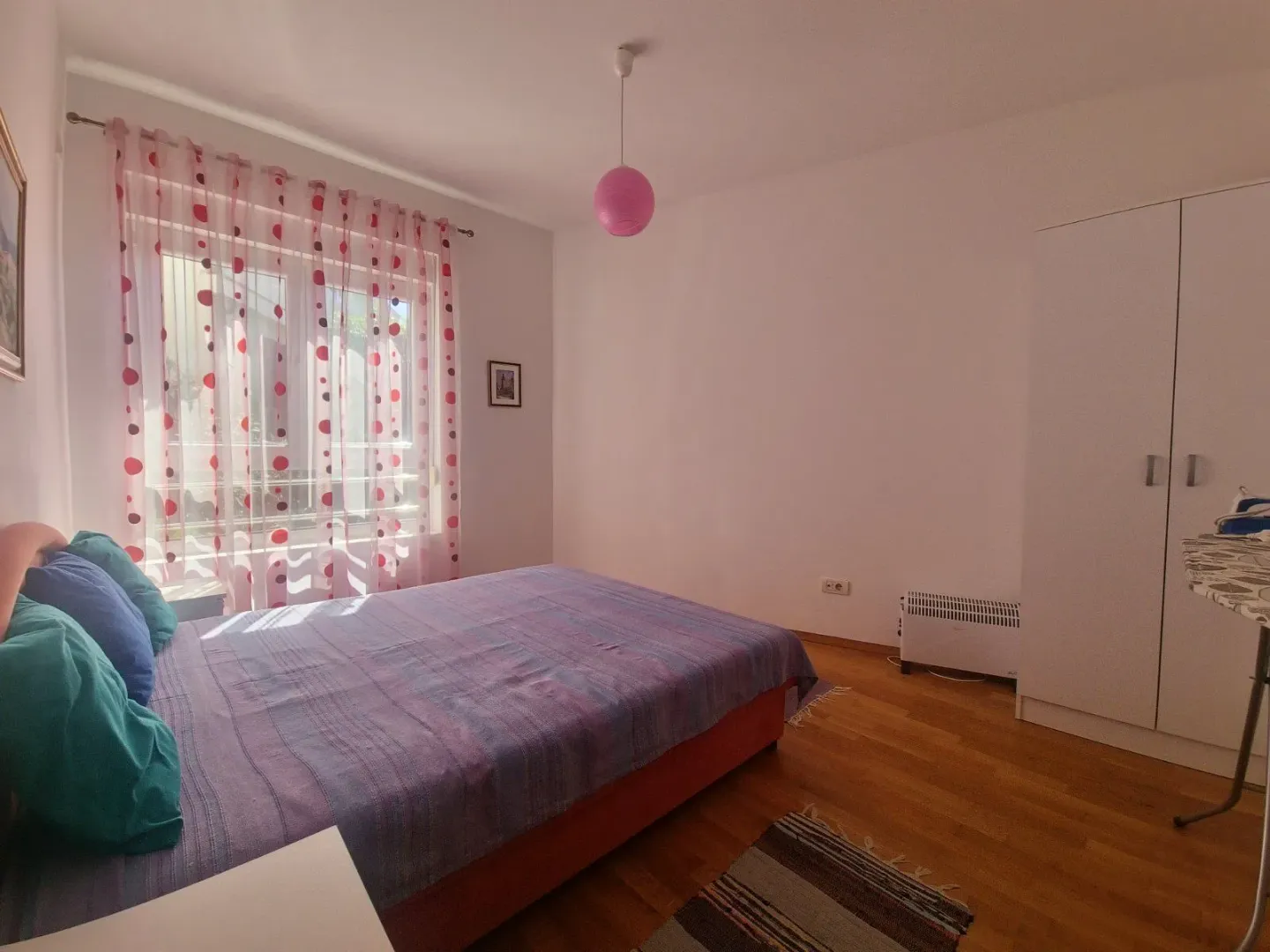 Spavaća soba sa bračnim krevetom, bijelim garderoberom i prozorom sa zavjesama.