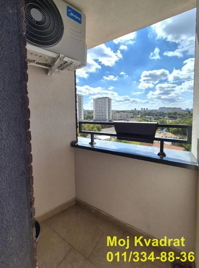 Manji balkon sa klima uređajem i pogledom na grad.