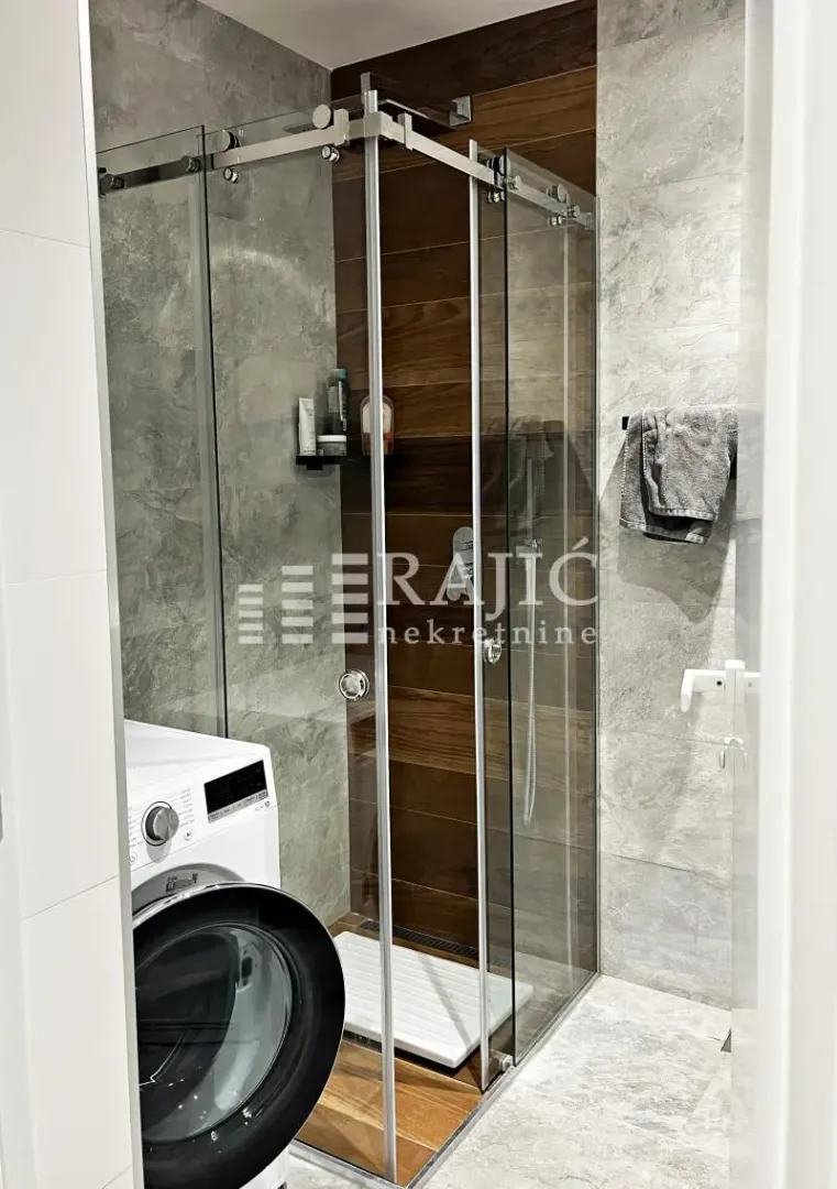 Modernly equipped bathroom with a shower cabin and washing machine.