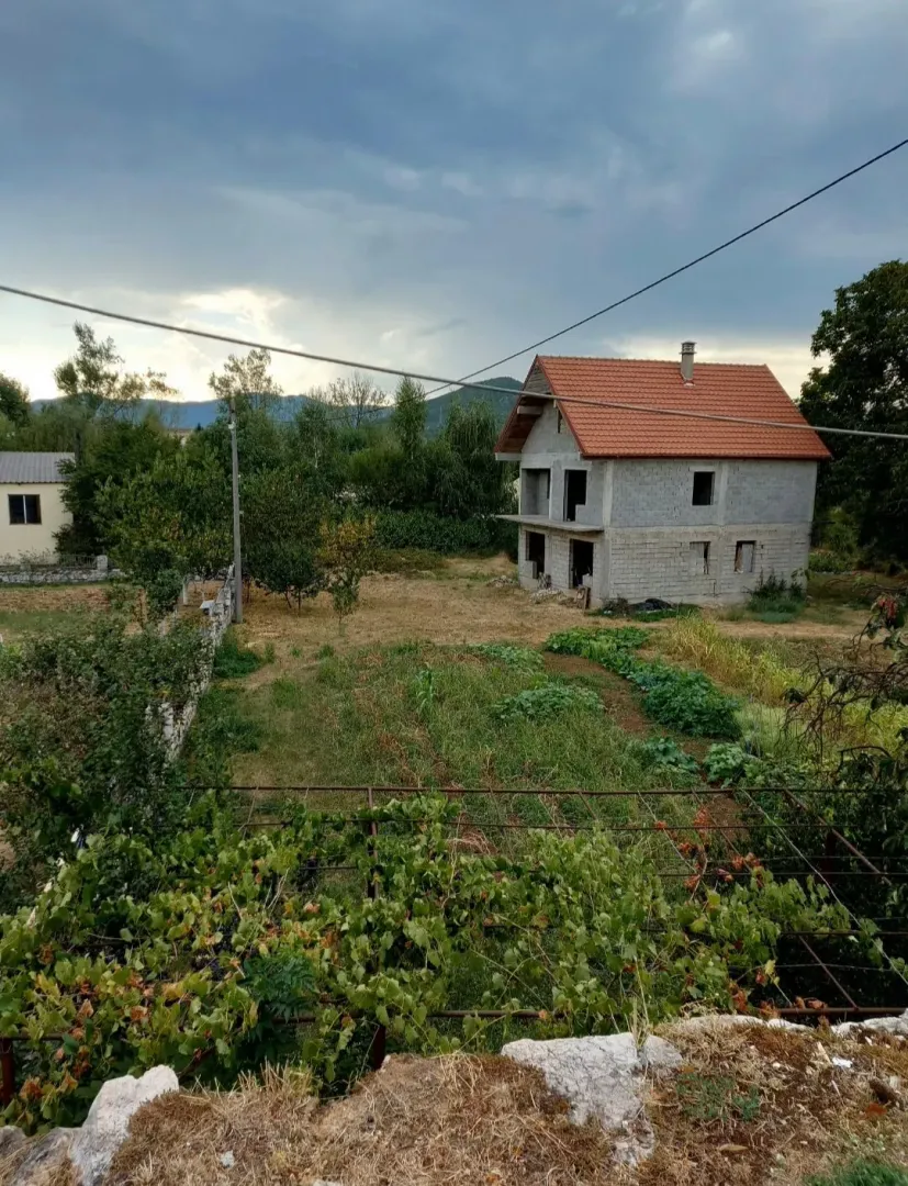 Pogled na kuću u izgradnji sa dvorištem i zelenilom.