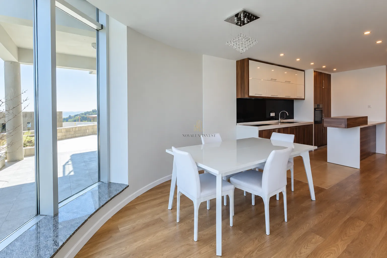 Dining area with a white table and chairs next to a modern kitchen and large windows.
