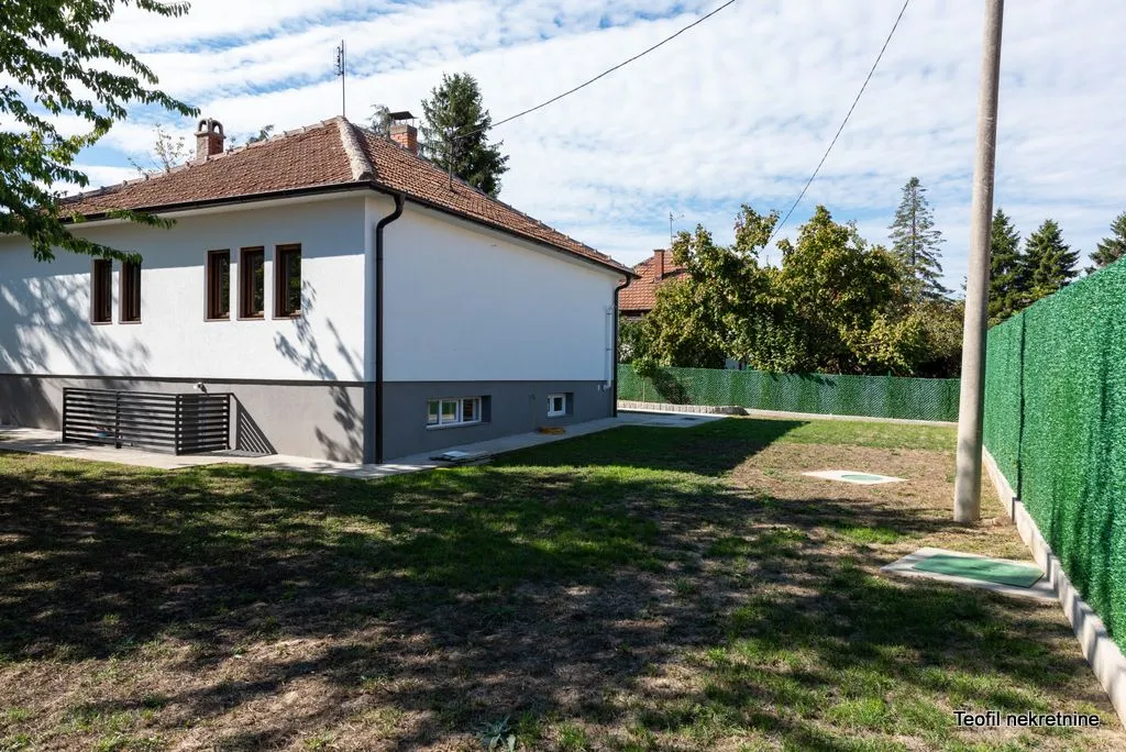 Pogled na dvorište i bočnu fasadu kuće sa uređenom travnatom površinom.