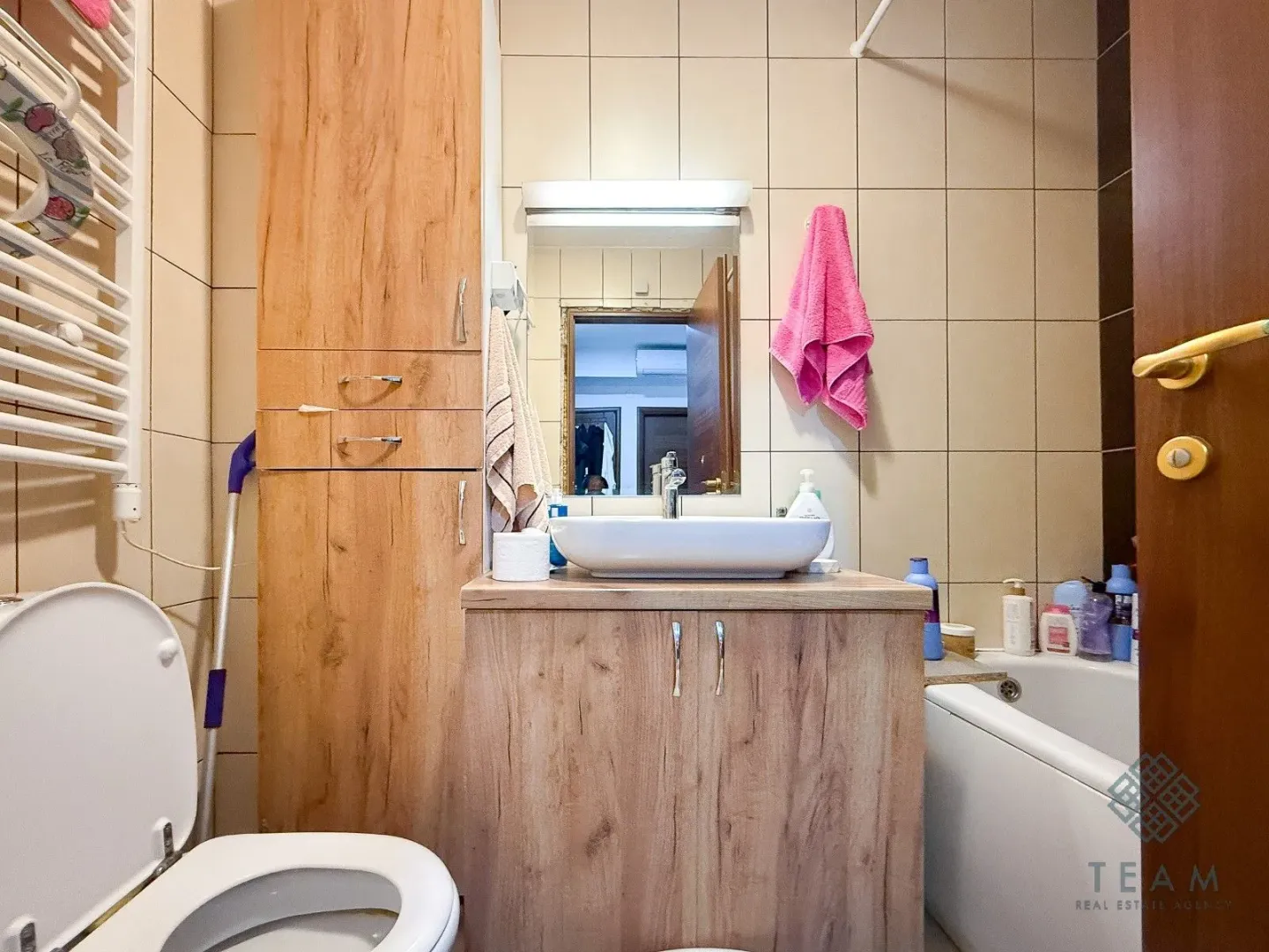 Kupatilo opremljeno umivaonikom sa ormarićem, wc šoljom, kadom i drvenim elementima.