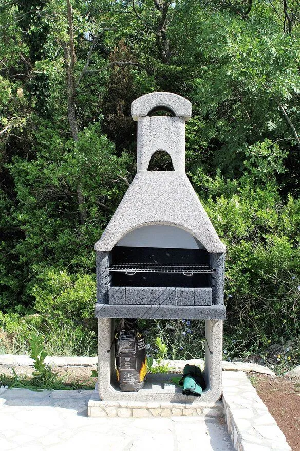 Concrete barbecue grill in the yard surrounded by greenery.