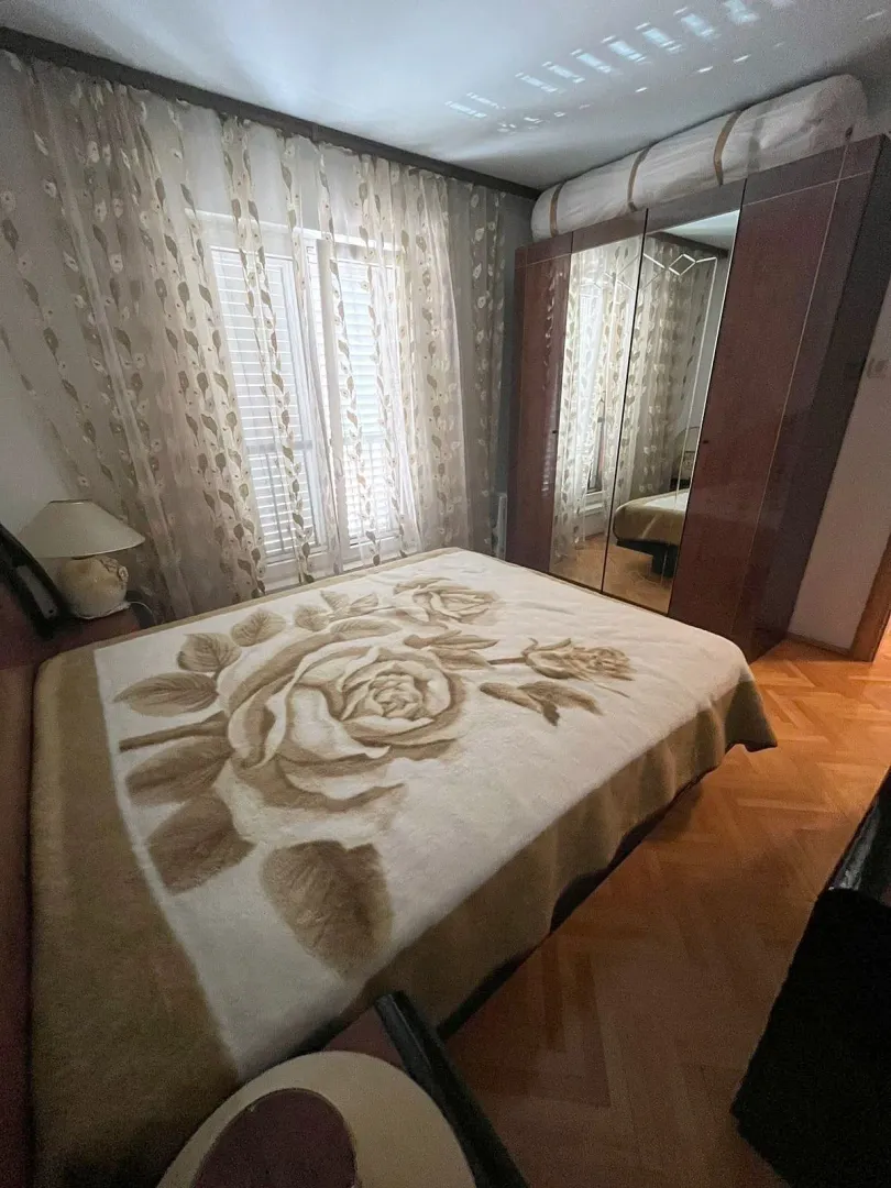 Spavaća soba sa bračnim krevetom, velikim ormarom i prozorom sa zavjesama.