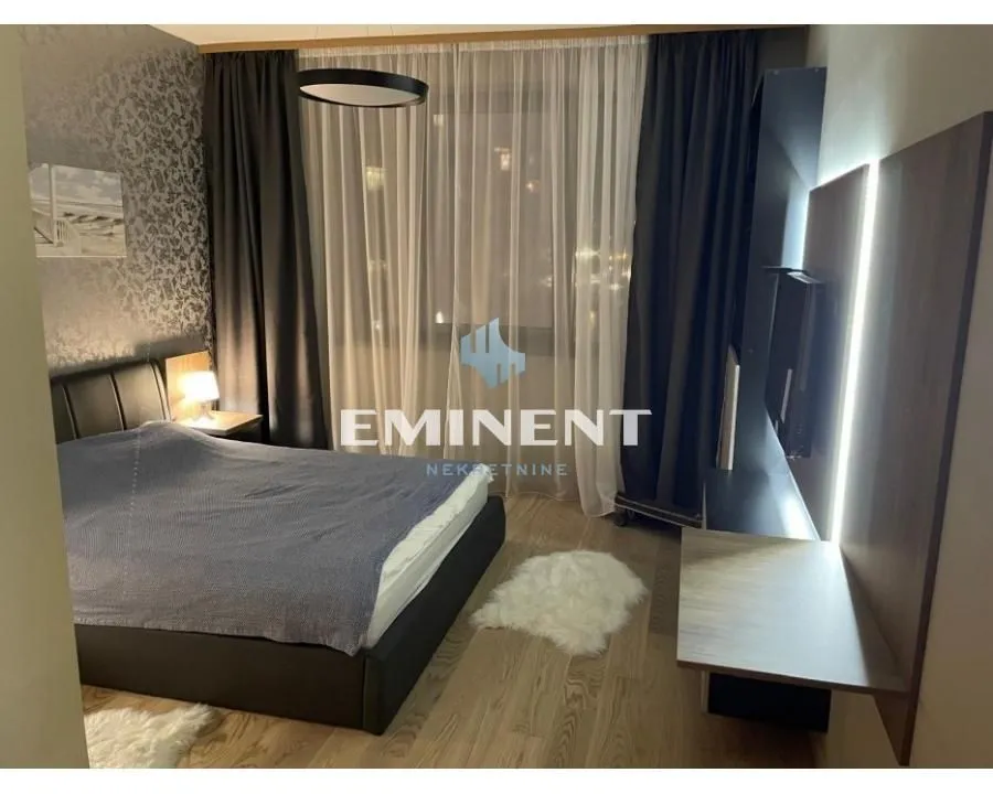 Furnished bedroom with a double bed, TV, and curtains.