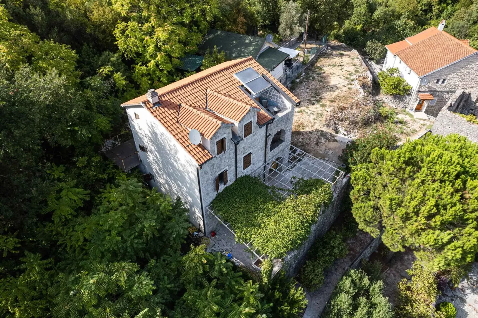 Pogled iz vazduha na tradicionalnu kamenu kuću sa okolinom i zelenilom.