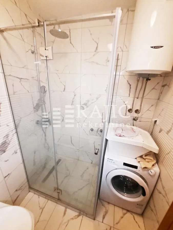Smaller bathroom with a shower cabin and washing machine.