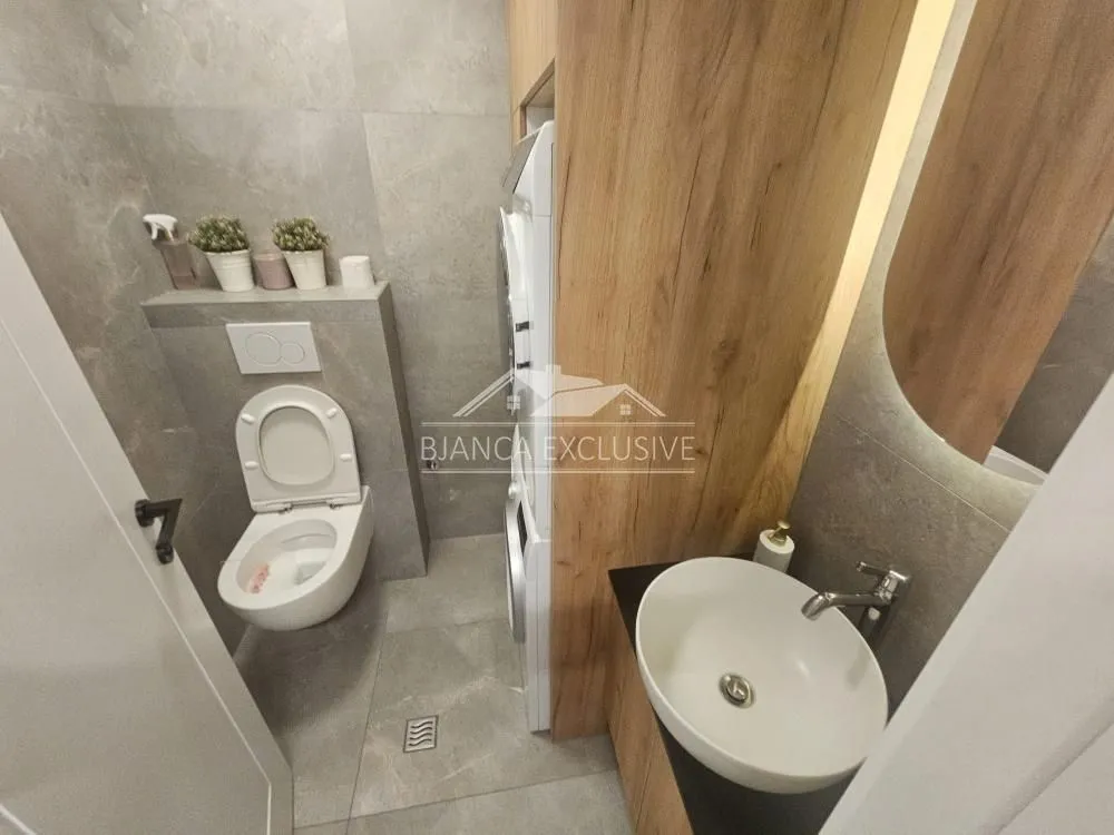 Moderno opremljeno kupatilo sa wc šoljom, umivaonikom i ugradnom mašinom za veš.