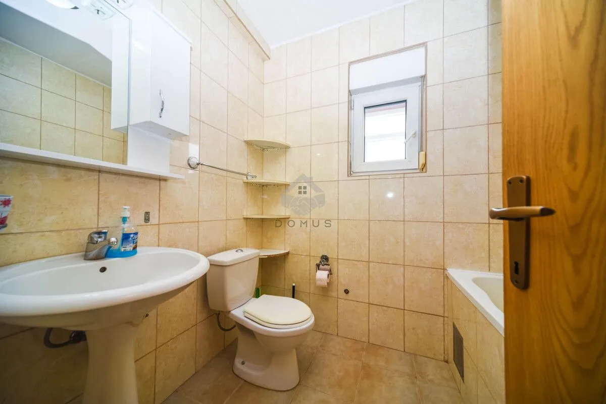 Kupatilo opremljeno umivaonikom, WC šoljom, kadom i zidnim ormarićem sa ogledalom.