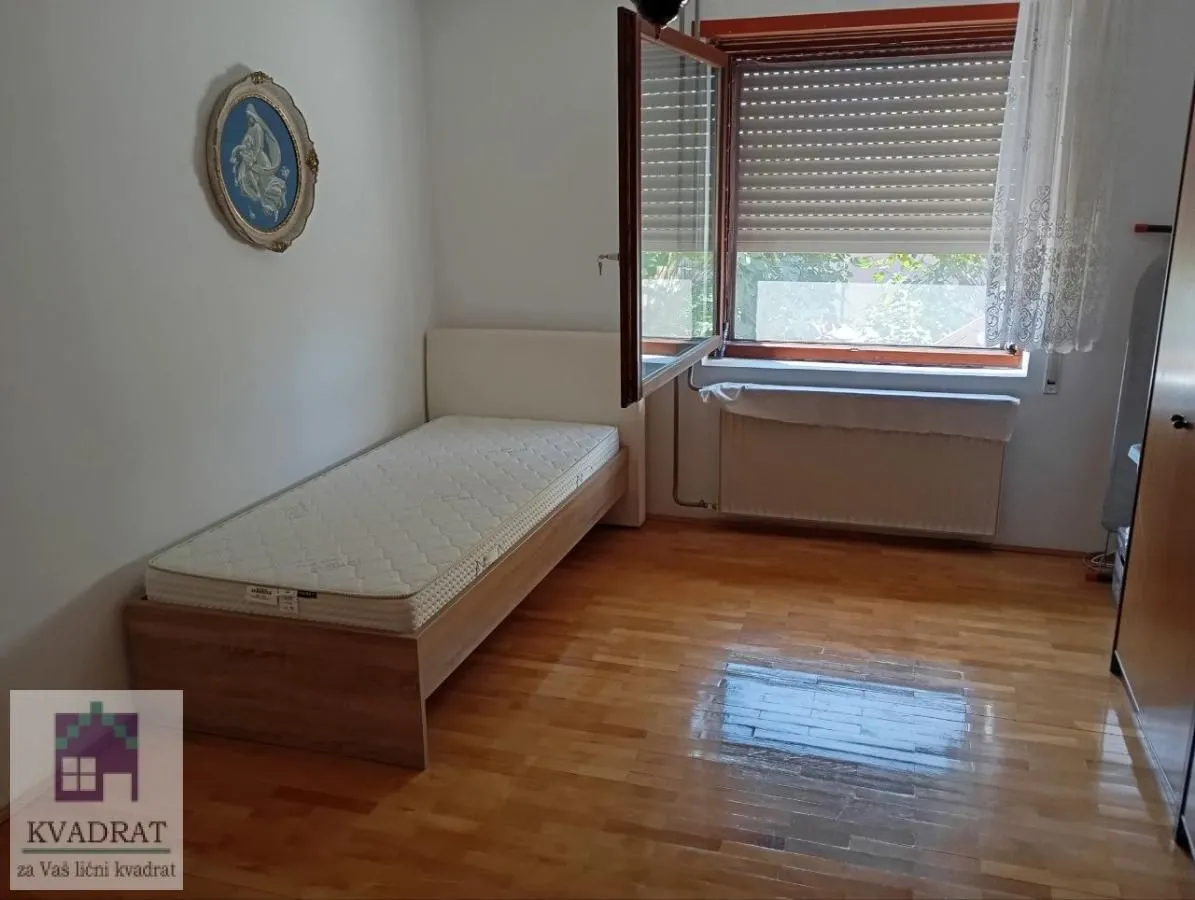Manja spavaća soba sa krevetom, drvenim parketom i prozorom.