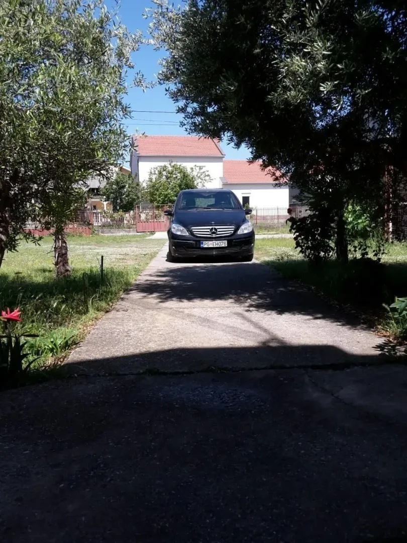 Dvorište sa prilaznim putem i parkiranim automobilom ispred kuće.