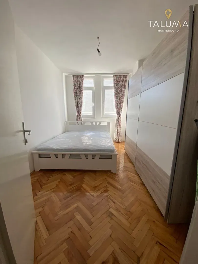 Furnished bedroom with a double bed, large wardrobe, and parquet flooring.