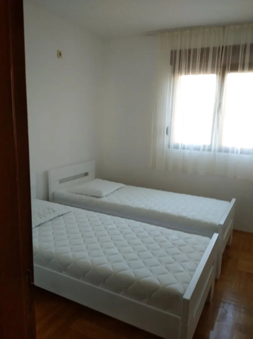 Spavaća soba sa dva odvojena kreveta i prozorom sa zavjesama.