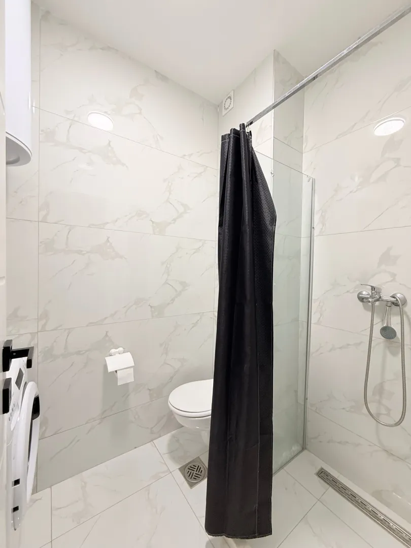 Moderne svijetle pločice u kupatilu sa tuš kabinom i wc šoljom.