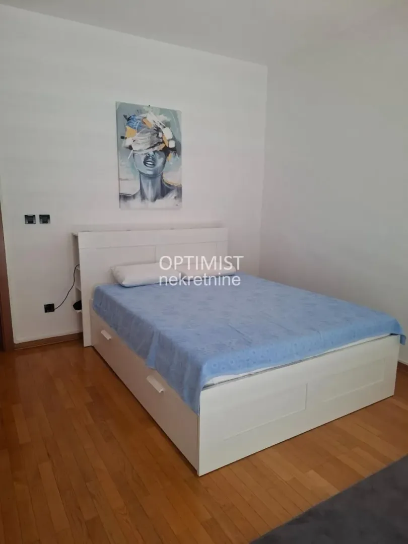 Spavaća soba sa bračnim krevetom i umetničkom slikom na zidu.