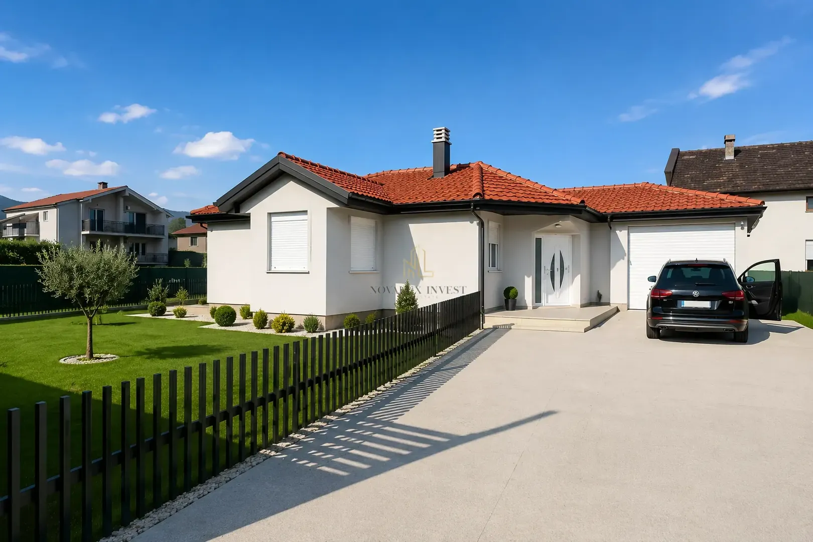 Pogled na prednju fasadu prizemne kuće sa uređenim dvorištem i parkingom.