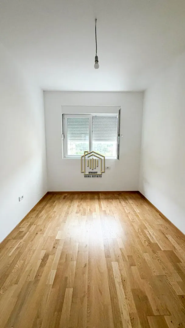 Prazna neopremljena prostorija sa drvenim podom i prozorom.