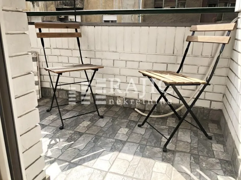 Small enclosed balcony with two wooden chairs.